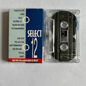 May include: A blue and white cassette tape with the text "SELECT 12" and a list of artists including House of Love, James, Yello, Electribe 101, Walker Brothers, The Hummingbirds, Ruby Blue, The Lilac Time, Dusty Springfield, Tom Verlaine, The Fall, and Cameo. The text "FREE WITH THE LAUNCH ISSUE OF SELECT" is printed at the bottom.