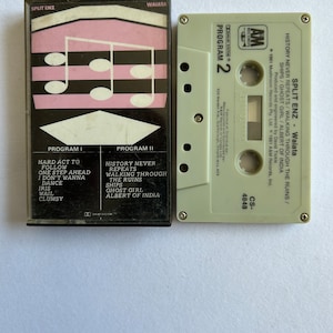 May include: A cassette tape with a black and white image of musical notes on the front. The tape is labeled "Split Enz - Waiata" and features the song titles "History Never Repeats" and "Walking Through The Ruins".