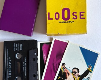 May include: A collection of music memorabilia featuring a cassette tape and related items. The black cassette tape is labelled "THERAPY?" and has song titles. A yellow box with "LOOSE THERAPY?" is present, alongside a purple box and small cards with images.