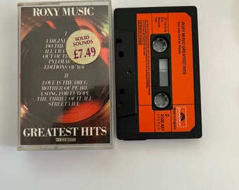 Może przedstawiać: Czarna kaseta z pomarańczową etykietą. Etykieta zawiera napis "ROXY MUSIC GREATEST HITS" i ma cenę "SOLID SOUNDS £7.49". Kaseta znajduje się w plastikowym pudełku z obrazkiem zespołu na przodzie.