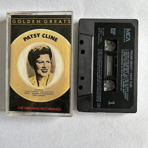 May include: A black cassette tape with a white label that reads "Golden Greats - Patsy Cline". The label also includes a list of songs on the tape, including "Walkin' After Midnight", "I Fall to Pieces", "Crazy", "Who Can I Count On", "She's Got You", "Strange", "When I Get Thru With You", and "Imagine What". The tape is from MCA Records and was released in 1979.