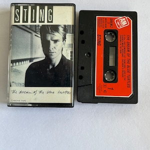 Op de afbeelding: Een zwarte cassetteband met een rood label. Het label heeft de tekst "The Dream of the Blue Turtles" en "Sting" erop. De cassetteband is een chroome band.