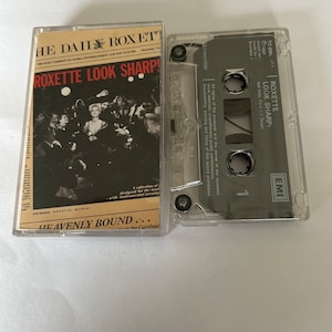 Puede incluir: Una cinta de casete con una foto en blanco y negro de una banda en la parte delantera. La cinta se titula "Roxette Look Sharp!" y presenta el texto "Heavenly Bound..." en la parte inferior. La cinta es de la marca EMI.