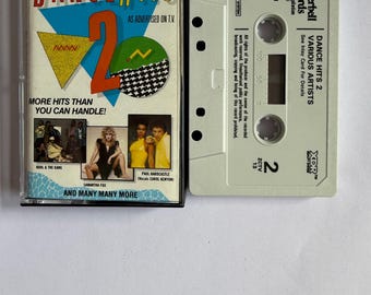 Może przedstawiać: Kasetę magnetofonową w stylu vintage "Dance Hits 2" z różnymi artystami. Okładka przedstawia kolorowe geometryczne kształty i tekst "More Hits Than You Can Handle!". Kaseta jest w kolorze złamanej bieli z "Towerbell Records."
