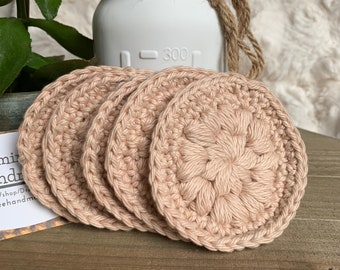Peut inclure: Quatre disques démaquillants réutilisables en crochet beige. Les disques sont ronds et présentent un motif floral au centre. Les disques sont empilés les uns sur les autres.