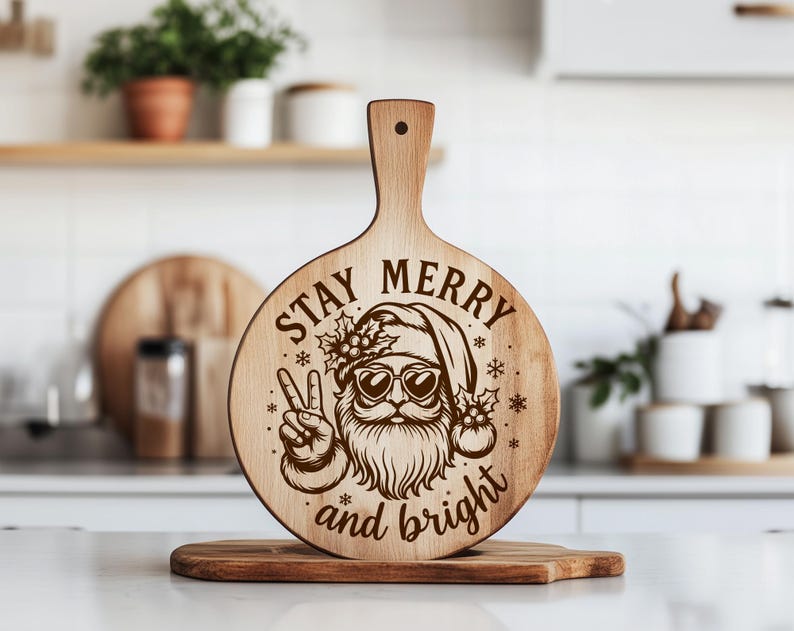May include: A wooden cutting board with a handle, featuring a laser-etched design of Santa Claus wearing sunglasses and giving a peace sign. The text "STAY MERRY and bright" is also etched on the board. The board is round with a handle.