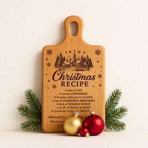 May include: A wooden cutting board with a handle, engraved with a Christmas recipe and a winter village scene. The board is decorated with pine sprigs and gold and red Christmas ornaments.