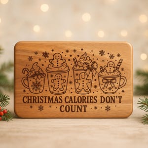 May include: A rectangular wooden cutting board with rounded corners. The board features engraved illustrations of four mugs with whipped cream, gingerbread men, and candy canes. The text "CHRISTMAS CALORIES DON'T COUNT" is also engraved.