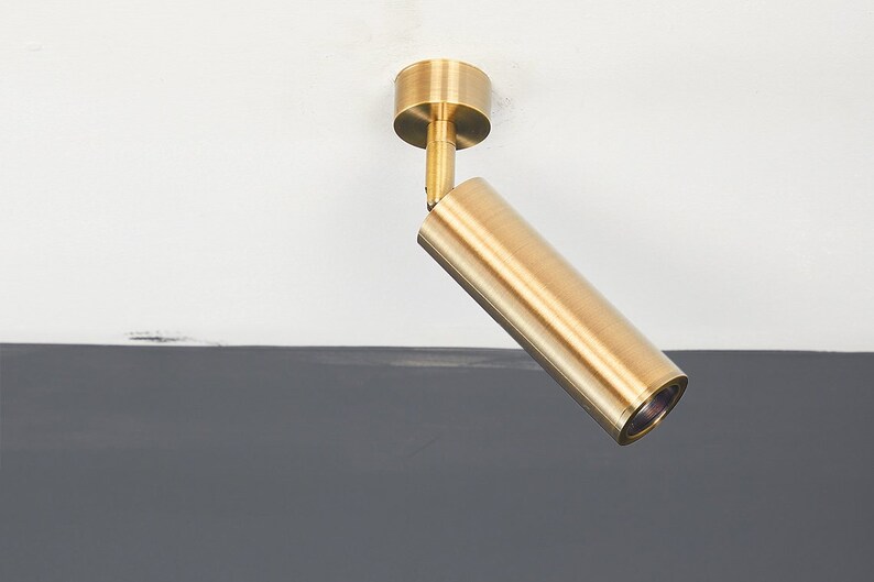 May include: A gold-toned ceiling spotlight with a cylindrical design. The light is angled downwards.