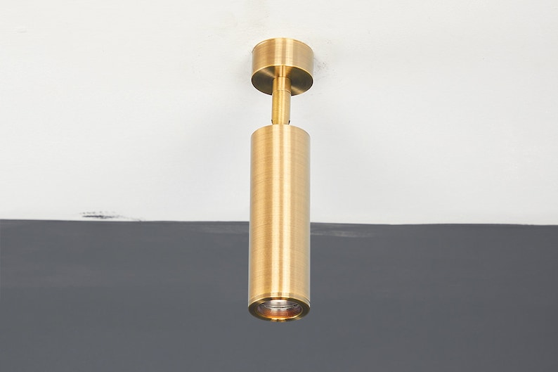 May include: A gold-toned cylindrical ceiling light fixture with a round, flat top.