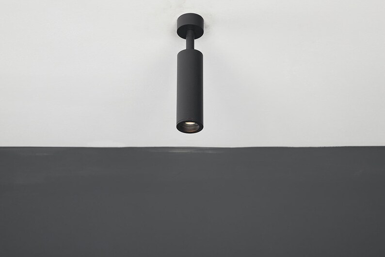 May include: A black cylindrical ceiling light fixture with a white light shining down.