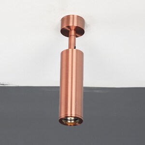 May include: A copper-colored ceiling light fixture with a cylindrical design. The light is mounted to the ceiling and has a round, frosted glass shade.