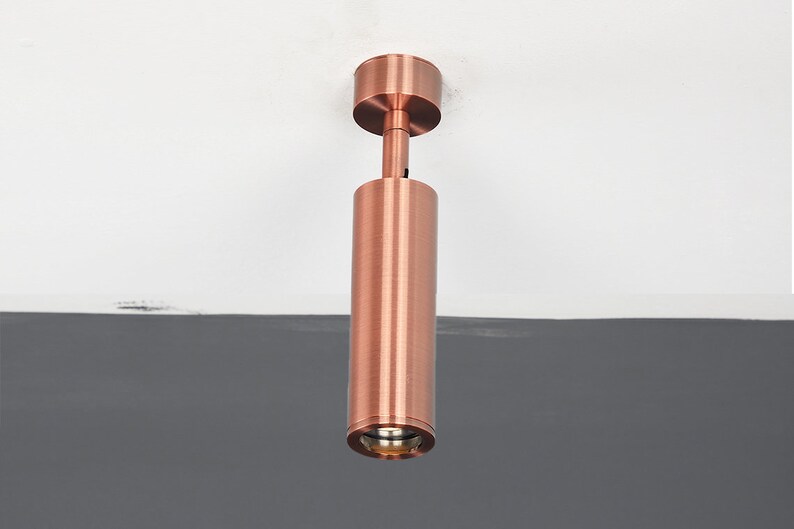 May include: A copper-colored ceiling light fixture with a cylindrical design. The light is mounted to the ceiling and has a round, frosted glass shade.