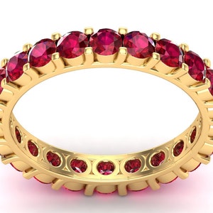 May include: A gold band ring with a row of red ruby gemstones.