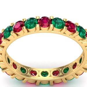 Op de afbeelding: Een gouden ring met afwisselende rode en groene edelstenen. De ring is bezet met ronde stenen en heeft een gepolijste afwerking.