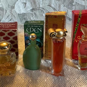 May include: A selection of vintage perfume bottles and their boxes. The bottles are in various shapes and colours, including a green bottle, a clear bottle with gold detailing, and a red bottle. The boxes are red, gold, and green, adding to the vintage aesthetic.