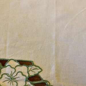 Puede incluir: Un mantel de lino blanco con un dise&ntilde;o floral bordado en verde alrededor de los bordes.