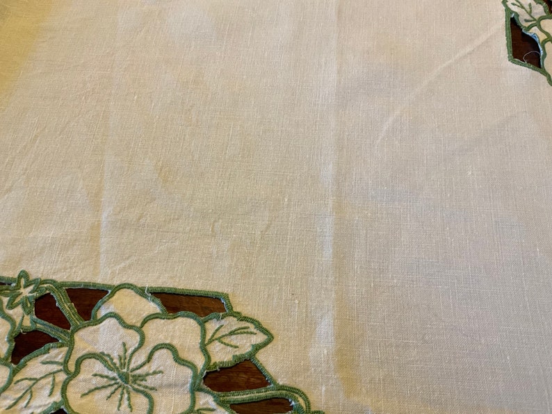 Puede incluir: Un mantel de lino blanco con un dise&ntilde;o floral bordado en verde alrededor de los bordes.