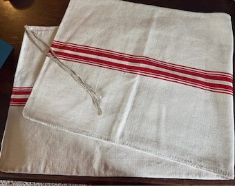 May include: Two off-white linen pillow covers with red stripes. The pillow covers have a simple design and are made of a natural fabric.