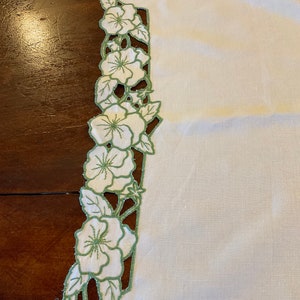 Puede incluir: Mantel de mesa de lino blanco con un dise&ntilde;o floral bordado en verde en el borde.