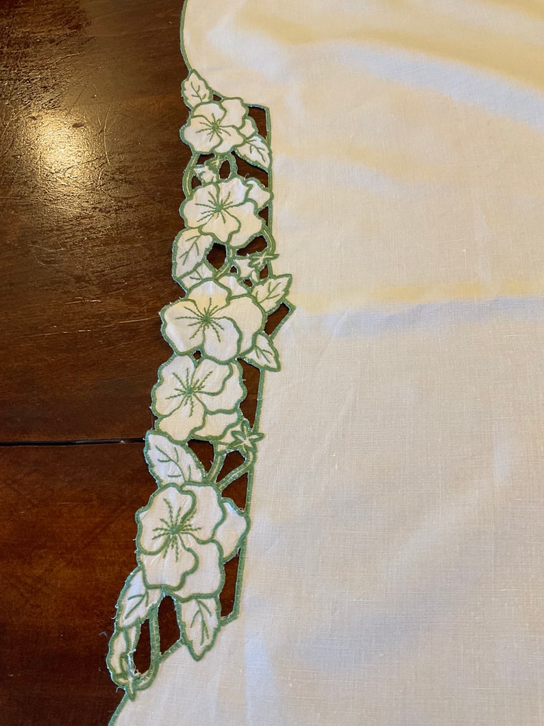 Puede incluir: Mantel de mesa de lino blanco con un dise&ntilde;o floral bordado en verde en el borde.