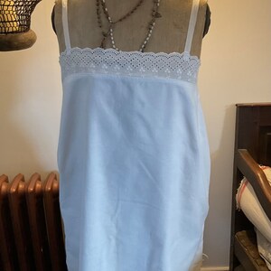 May include: A white cotton slip with a lace trim. The slip is on a vintage-style dress form with a beaded necklace.