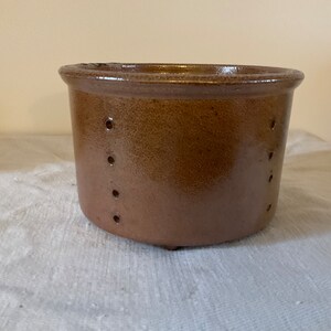 以下が含まれることがあります： 側面に穴が開いた茶色の陶器の鉢。鉢は丸い底とわずかに広がった縁をしています。