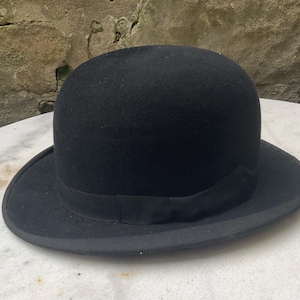 Può includere: Un cappello bombino in feltro nero con un'ampia tesa. Il cappello ha un nastro in grosgrain nero attorno alla corona.