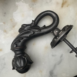 May include: A dark bronze door handle with a dragon head design. The handle has a curved grip and a floral base. The mounting hardware includes a round backplate and a threaded bolt. The handle is made of metal and is suitable for doors.