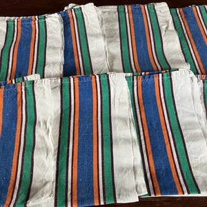 May include: Several folded napkins with a light background and vertical stripes in blue, green, orange, and white. The napkins are made of a soft material, suitable for a kitchen or dining room.