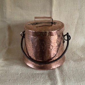 Peut inclure: Une casserole en cuivre martelé avec un couvercle et une poignée en fer noir. La casserole a un aspect rustique et antique.