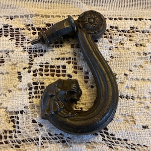 May include: Black cast iron hook with a decorative lion head and a floral design. The hook is attached to a metal screw.