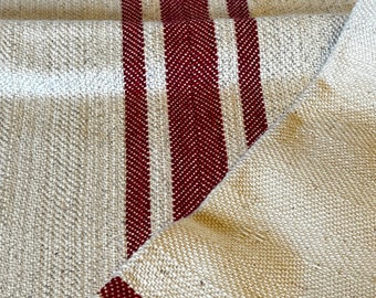 May include: A close-up of a natural linen fabric with three red stripes running vertically. The fabric is folded in half, showing the stripes on both sides.