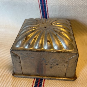 Op de afbeelding: Een vintage zilveren metalen cakevorm met een geribbeld ontwerp. De vorm heeft een vierkante basis en een gewelfde bovenkant.