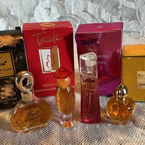 May include: A collection of miniature perfume bottles and boxes. Brands include First by Van Cleef & Arpels, Tocade, Very Irresistible Givenchy, and Sublime by Jean Patou. The bottles are various shapes and sizes, with gold and silver accents.