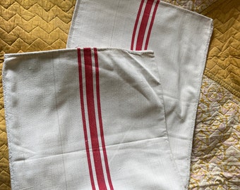 May include: Two white linen tea towels with red stripes. The towels are folded and stacked on top of each other.
