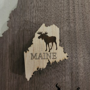 May include: A wooden cutout of the state of Maine with a moose silhouette and the word "MAINE" engraved on it.