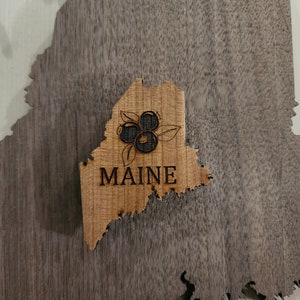 May include: A wooden cutout of the state of Maine with the word "MAINE" and a depiction of blueberries.