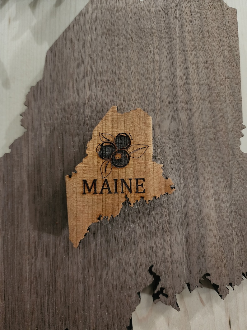 May include: A wooden cutout of the state of Maine with the word "MAINE" and a depiction of blueberries.