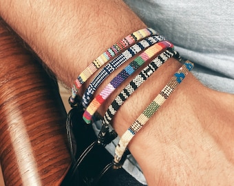 Peut inclure: Un poignet d'homme avec cinq bracelets tissés colorés. Les bracelets sont faits de fils de différentes couleurs et sont empilés les uns sur les autres.