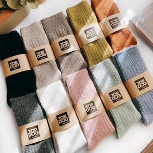Könnte beinhalten: Eine Auswahl an farbenfrohen Socken in verschiedenen Farbtönen, darunter Schwarz, Grau, Rosa und Grün. Jedes Paar ist mit einem braunen Papierband mit dem Logo "TOP DOG LONDON" umwickelt. Die Socken scheinen aus geripptem Strickmaterial zu sein.