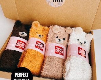 May include: Four pairs of fuzzy animal-themed socks in a cardboard gift box. Each pair features a bear face with ears and a pink paper band labeled Top Dog London. The box lid has a circular sticker that reads Hug in a Box.