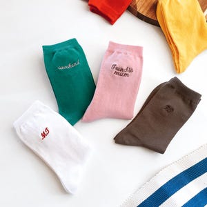 May include: A collection of five pairs of socks in various colours including white with red MJ embroidery, green with white weekend embroidery, pink with brown Frenchie mum embroidery, brown with brown HJ embroidery, red, and yellow.