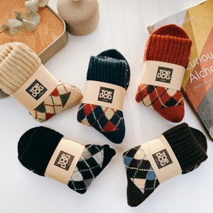 May include: Five pairs of argyle patterned socks in beige, navy, rust, black, and brown. Each pair is wrapped with a brown paper band featuring the "TOP DOG LONDON" logo. The socks are displayed on a white surface.