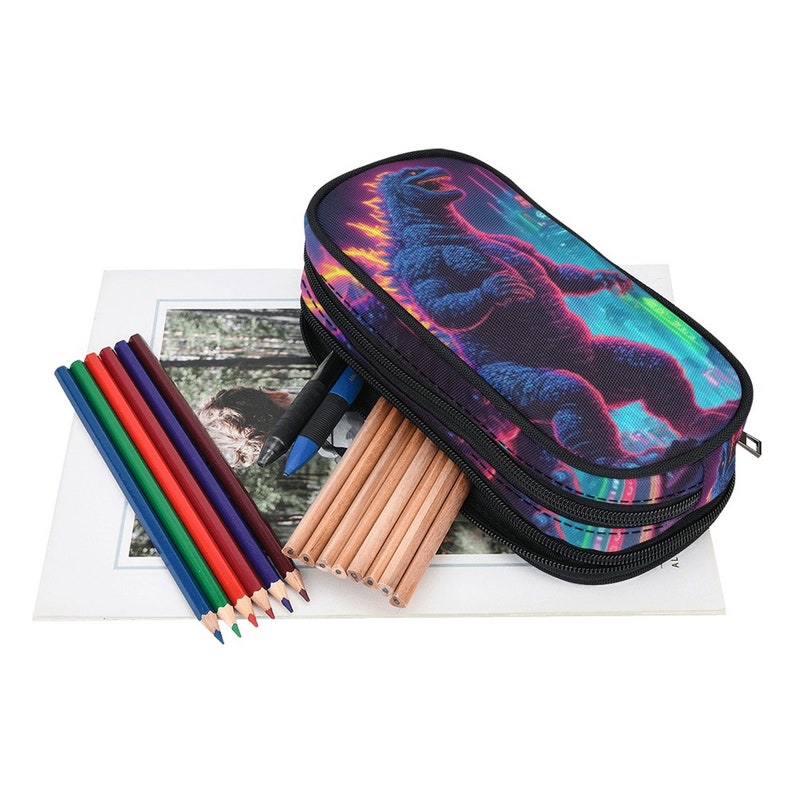 May include: A black pencil case with a zipper closure features a colorful graphic print of a Godzilla-like monster. The case is open and filled with colored pencils and pens.