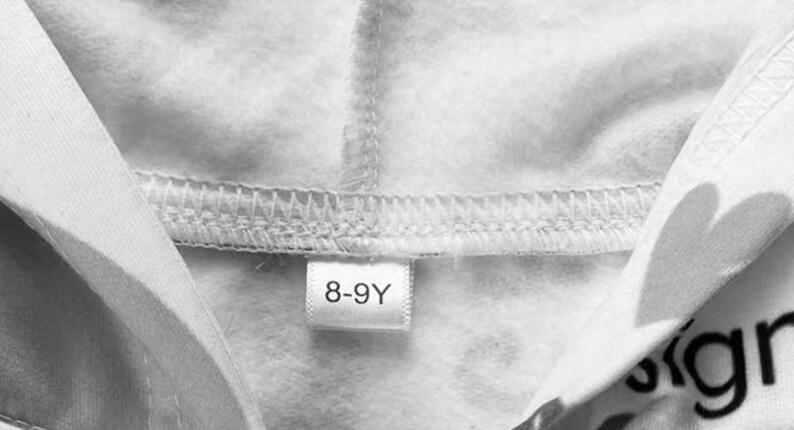 Op de afbeelding: Witte hoodie met een maatlabel met de tekst "8-9Y".