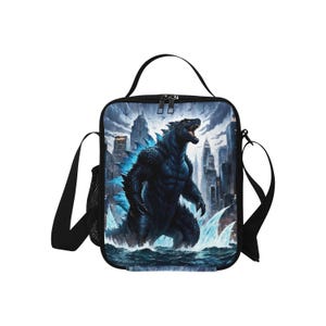 May include: Black lunch bag with a Godzilla graphic. The bag features a black monster with blue accents standing in a city with water in the foreground. The bag has a black adjustable shoulder strap.