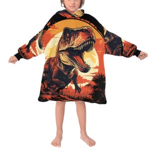 May include: A black hooded blanket with a large orange and red dinosaur illustration. The dinosaur is a Tyrannosaurus Rex with a sunset background.