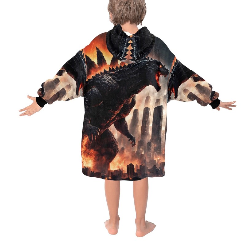 May include: A black and orange hooded blanket featuring a Godzilla graphic. The design shows Godzilla roaring in a city engulfed in flames. The blanket has long sleeves with black cuffs and a hood.