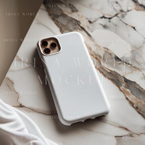May include: A white smartphone case with a gold camera lens frame rests on a marble surface. The phone case is the primary focus, with the marble adding a contrasting texture. The text "IRINA WORLD MOCKUP" is visible.